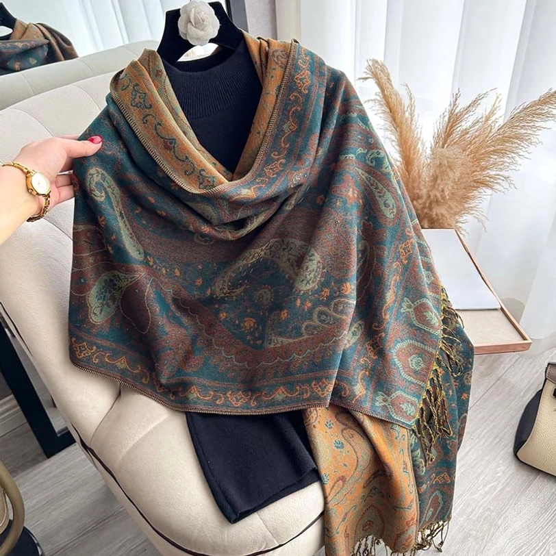 Close-up side view of teal mustard paisley pattern shawl with hand holding fringe trim