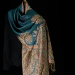Tibetan paisley tassel shawl with teal and gold floral jacquard pattern, draped over black knit sweater - front three-quarter view