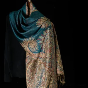 Tibetan paisley tassel shawl with teal and gold floral jacquard pattern, draped over black knit sweater - front three-quarter view
