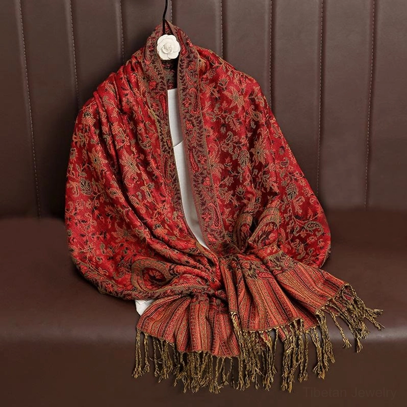 Red Tibetan ethnic shawl with golden jacquard paisley patterns displayed on brown leather sofa with tassels