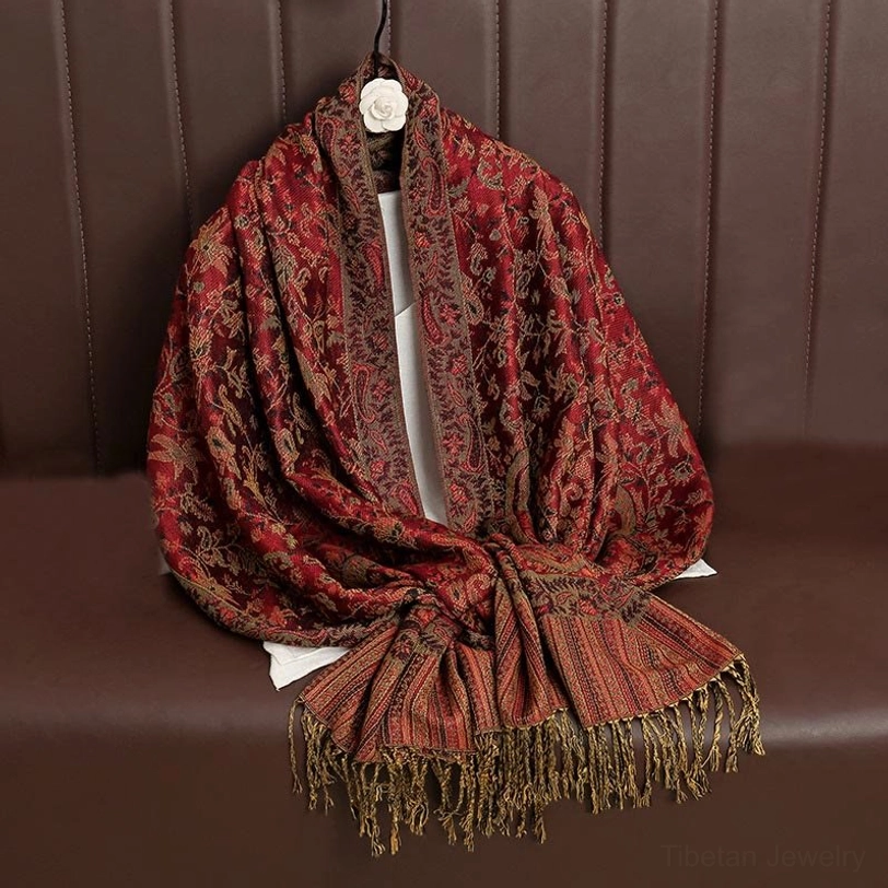 Deep reddish brown Tibetan ethnic shawl with golden paisley jacquard hanging on leather sofa with long tassels