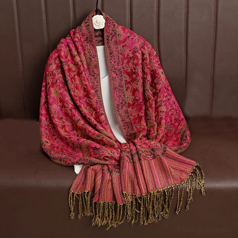 Rose red Tibetan ethnic shawl with golden paisley jacquard displayed front view on brown leather sofa with fringes