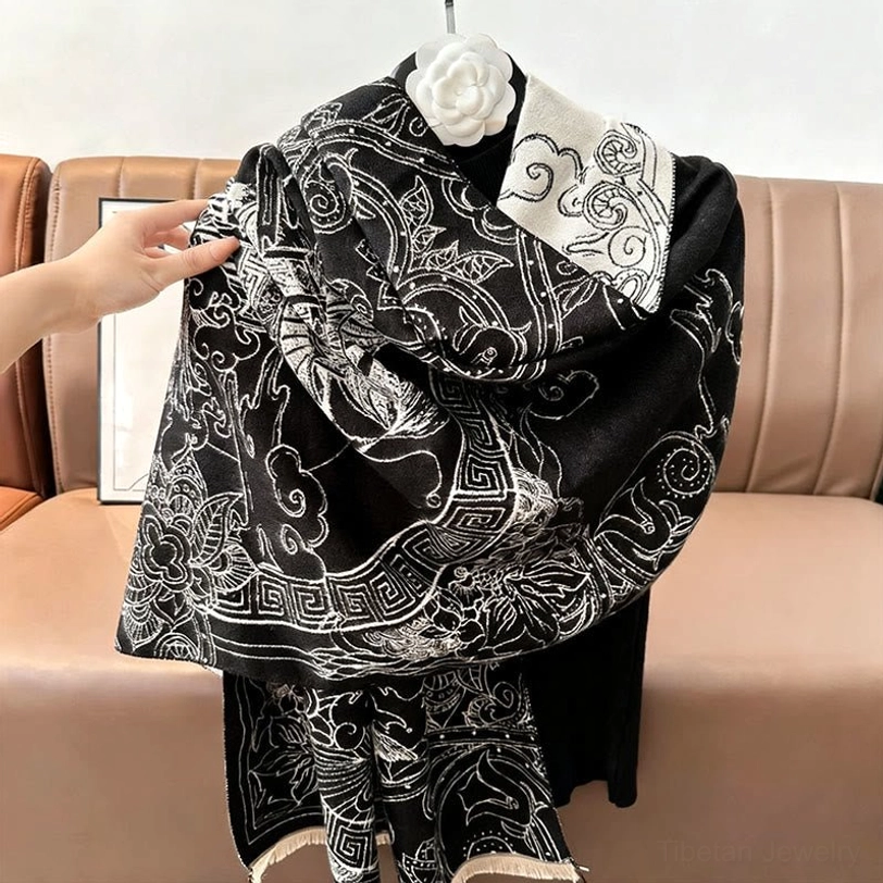 Tibetan pavilion scarf worn on mannequin with white brooch accent showing all-over black artistic print and reversed edge trim styling