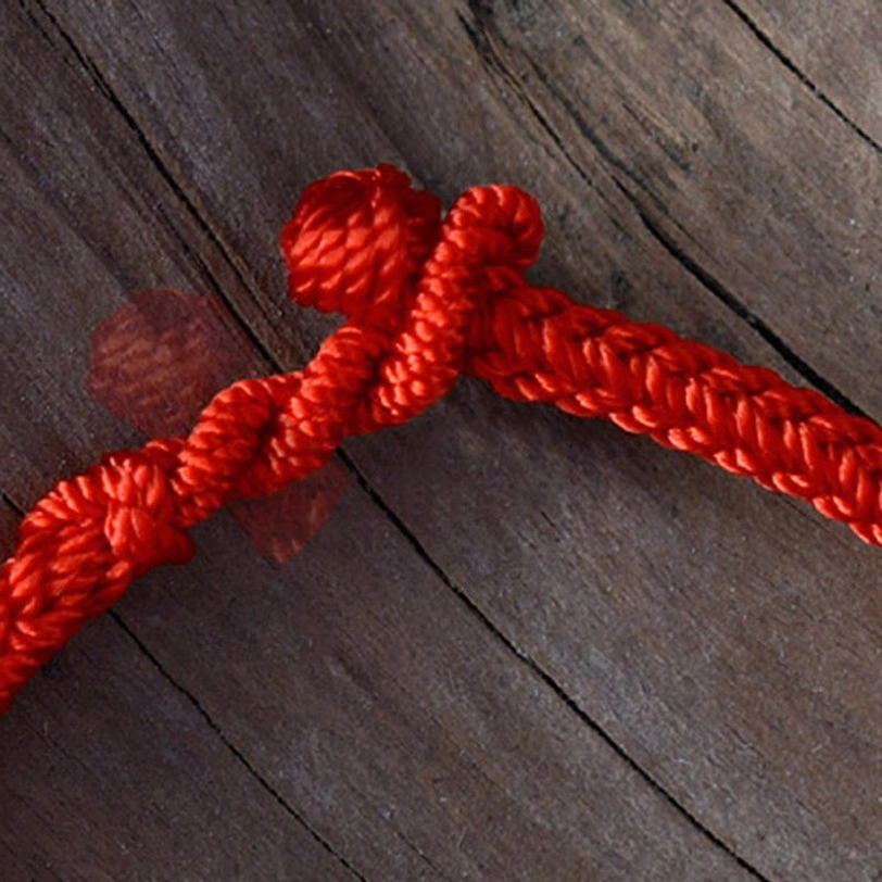 Extreme close-up of tibetan peace knot hand-tied decorative knot closure in red woven cord on wooden background