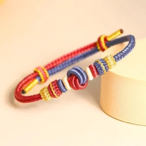 Handwoven Tibetan eight-thread peace knot bracelet in red and dark blue dual-tone, displayed on beige natural background with decorative elements