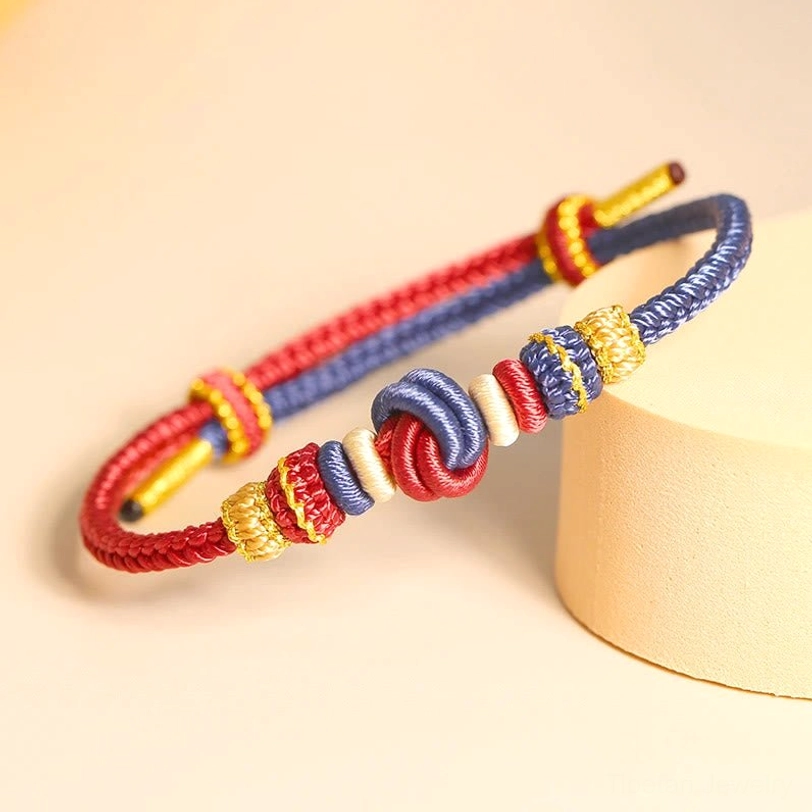 Handwoven Tibetan eight-thread peace knot bracelet in red and dark blue dual-tone, displayed on beige natural background with decorative elements