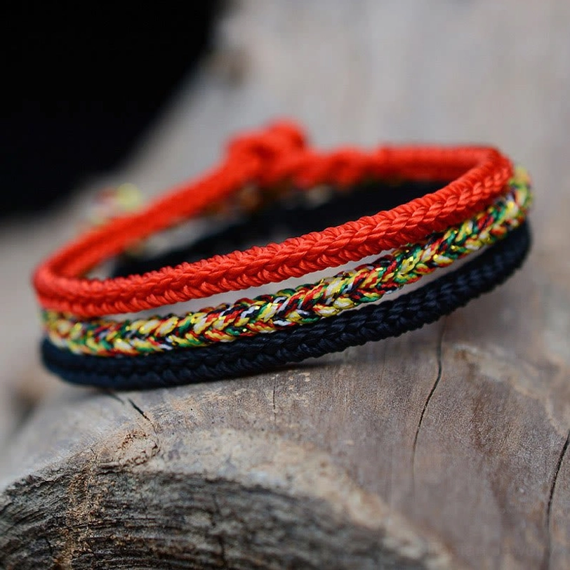 Close-up side view of handwoven eight-thread peace knot bracelet with red multicolor and black braided cords and adjustable knot