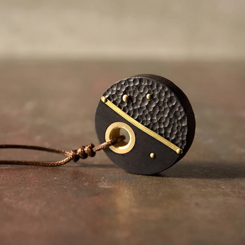 Ebony wood brass peace pendant displayed on table showing side profile and braided cord