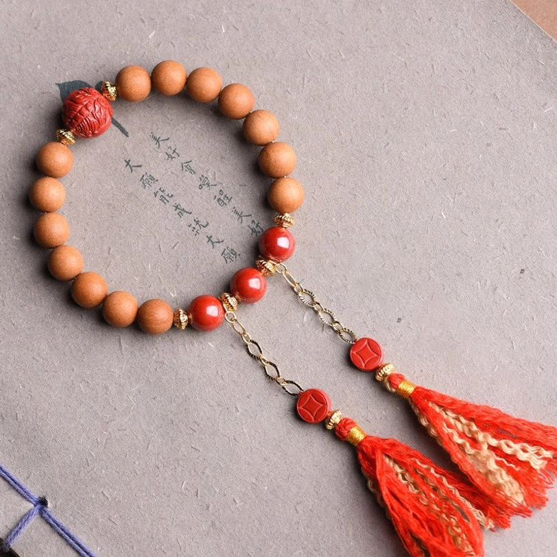 Tibetan peach wood pixiu cinnabar wealth bracelet with dual red silk tassels displayed on calligraphy paper, top-down flat lay view