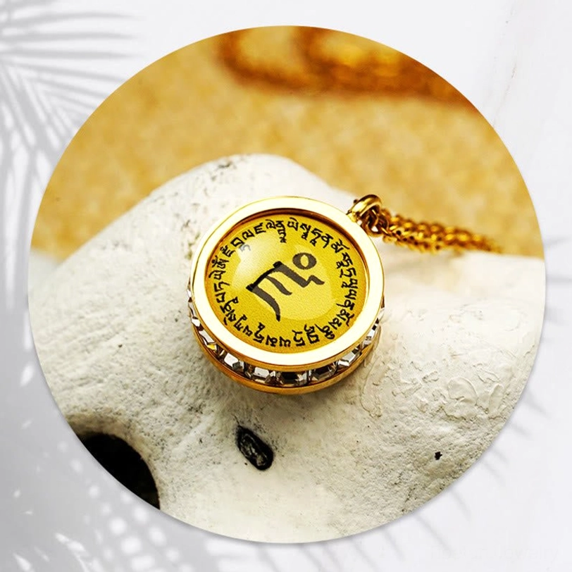 Top-down close-up of Tibetan mantra pendant necklace showing crystal-inlaid gold rim and yellow mantra base