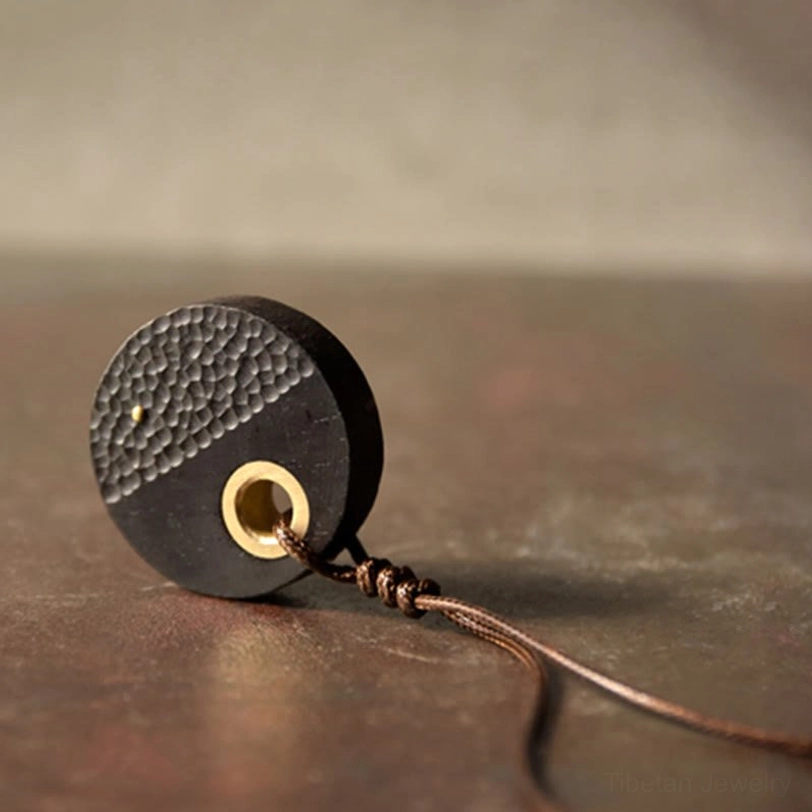Close-up side view of handcrafted ebony pendant highlighting brass hanging ring and braided rope