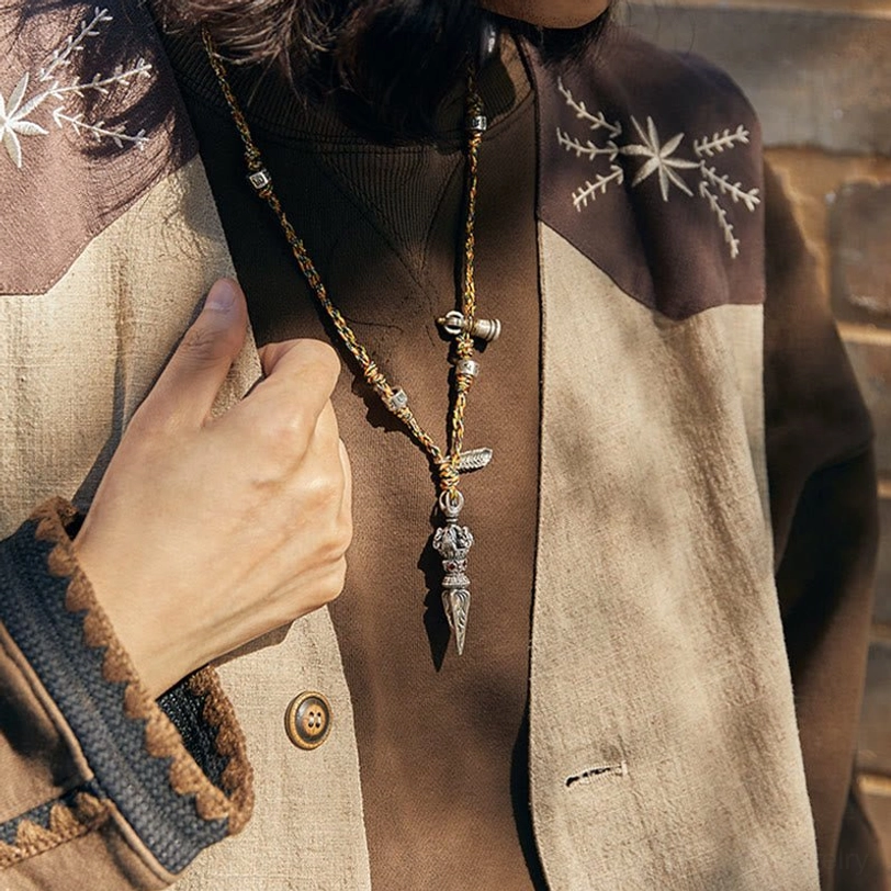 On-body close-up of Tibetan silver Dorje necklace showing adjustable braided rope and vintage silver hardware worn over embroidered jacket