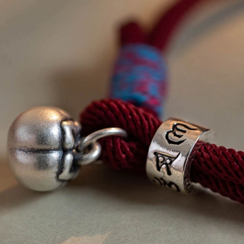 Macro close-up of persimmon-shaped silver bell charm and tibetan script engraved bead with colorful trim
