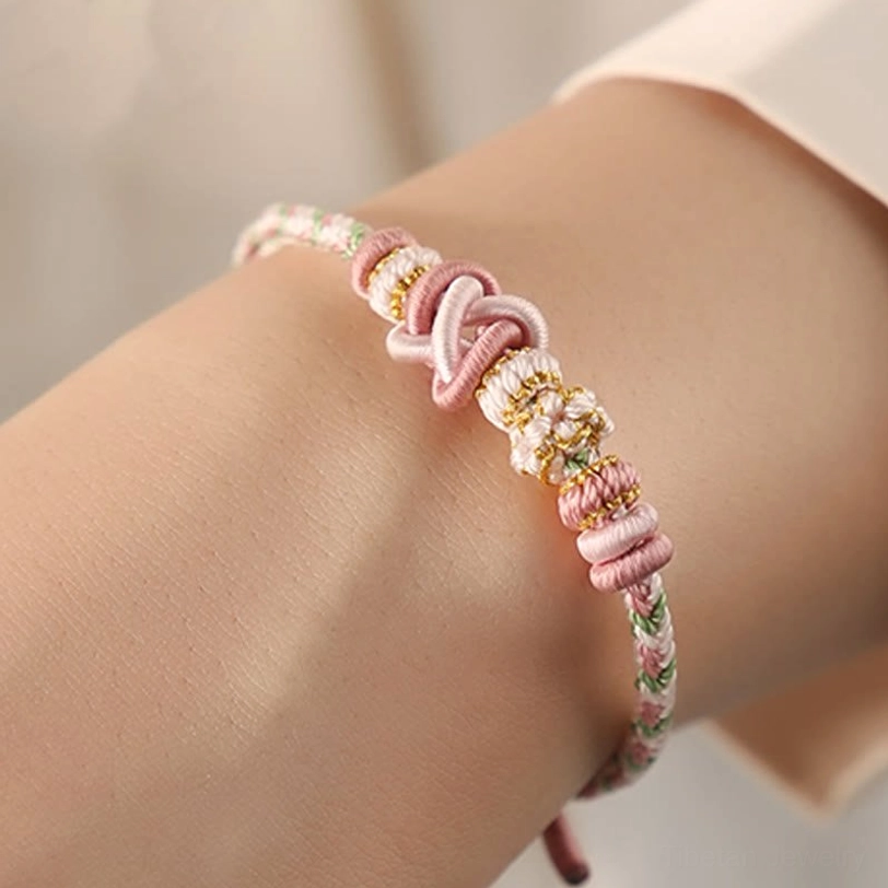 Pastel pink and light green tibetan peace knot bracelet worn on wrist showing delicate flower-shaped knots and adjustable fit