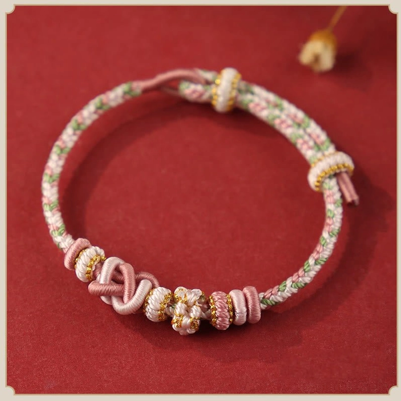 Pink peach blossom tibetan peace knot bracelet with light green and gold accents, handwoven floral design flat lay