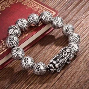 Tibetan Pixiu silver wealth bracelet with carved antique beads and protective charm displayed on wooden table