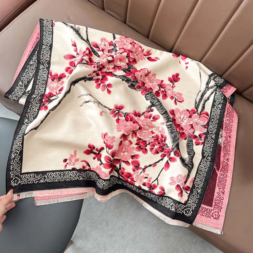 Beige Tibetan plum blossom scarf with pink-red floral prints and black vintage border held by hand on leather sofa