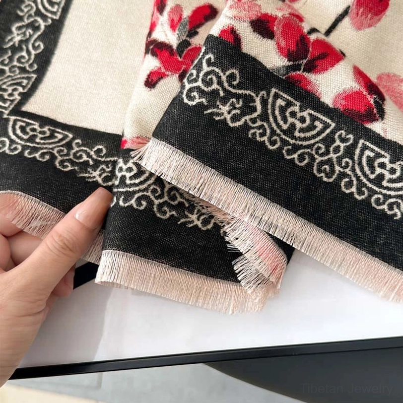 Close-up texture shot of Tibetan plum blossom scarf fabric showing vintage geometric border, tassel fringe, and woven quality