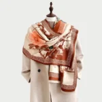 Tibetan plum blossom ink painting scarf in warm tones, styled on mannequin showcasing beige base with orange floral and pavilion print detail