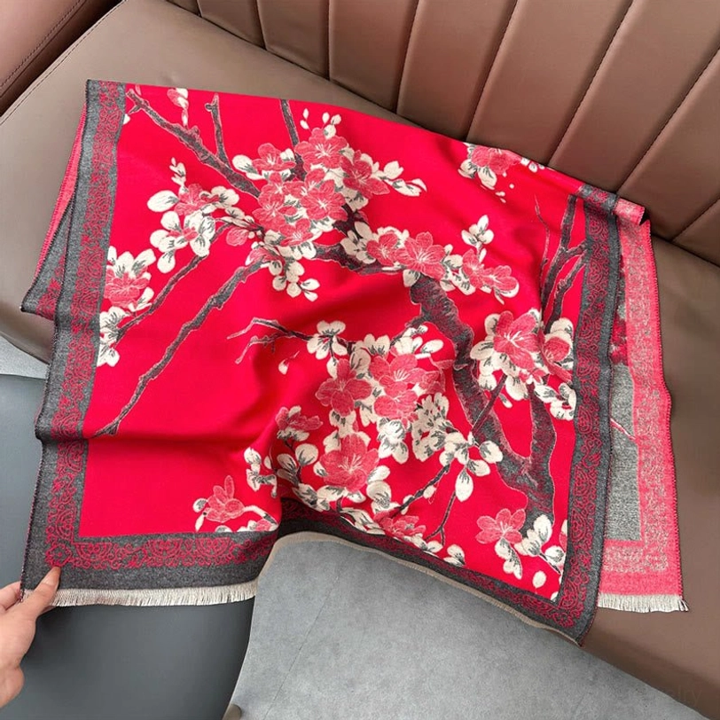 Overhead flat lay of red Tibetan plum blossom shawl on brown leather sofa showing full floral design and geometric border