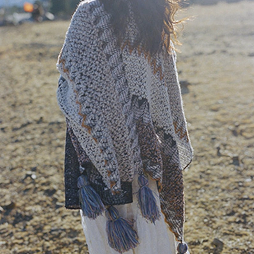 Front full-body walking view of Tibetan striped poncho shawl with blue tassel trims paired with white dress near stone cabin