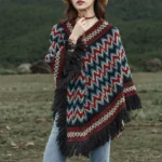 Tibetan striped knit poncho with tassel trim worn in outdoor grassland setting, front view showcasing chevron pattern and black fringe hem
