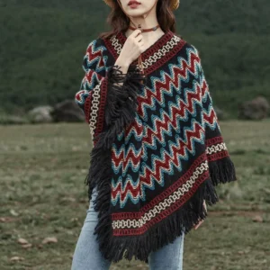 Tibetan striped knit poncho with tassel trim worn in outdoor grassland setting, front view showcasing chevron pattern and black fringe hem