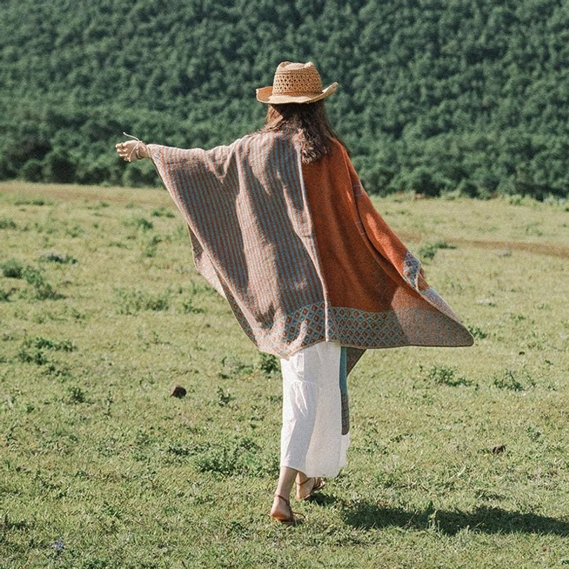 Back full view of oversized Tibetan winter poncho showing flowy draped hem and warm soft knit fabric on open grassland with forest
