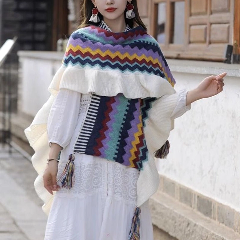 Model wearing Tibetan knit poncho shawl in courtyard setting with ruffled shoulder trim, side tassels and white dress