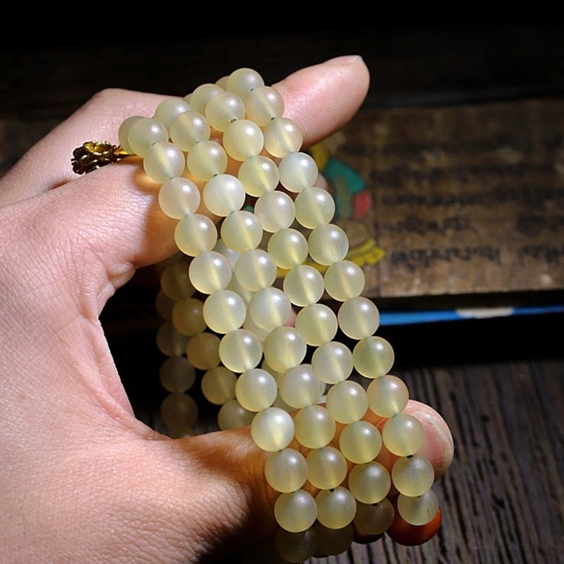 Finger holding individual Tibetan prayer beads showing smooth light yellow sheep horn beads and red ornament