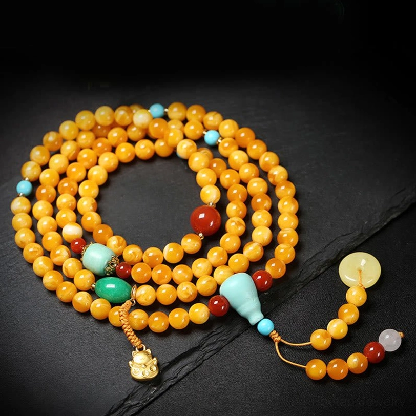 Overhead shot of 108-bead mala with yellow jade peace buckle gold metal pendant and mixed gemstone accents on slate surface