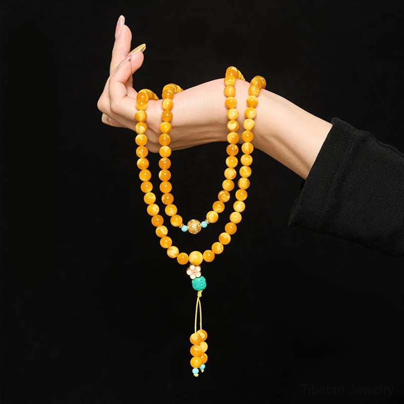 Double-strand Tibetan amber mala worn on left hand with spacer beads and dangling turquoise tassel pendant against black background