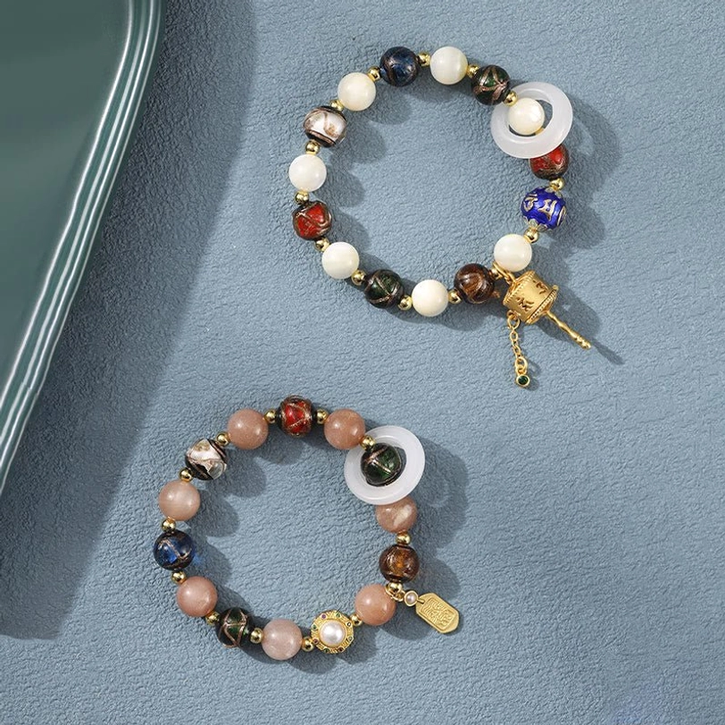 Two Tibetan spiritual bracelets featuring prayer wheels and mixed gemstone beads displayed together on gray surface