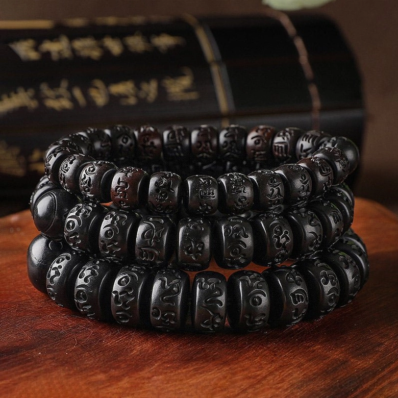 Multiple stacked Tibetan prayer bracelets displaying uniform dark wooden barrel beads with mantra carvings, high-angle arrangement on traditional backdrop