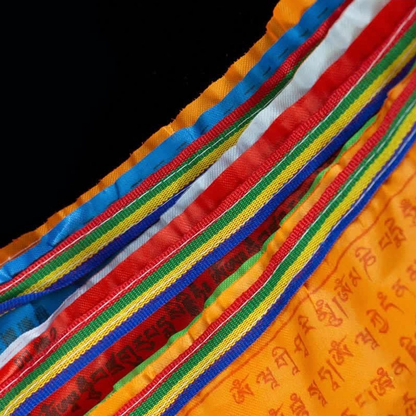 Extreme close-up of prayer flag fabric weave showing multi-color striped webbing and Tibetan script printing texture