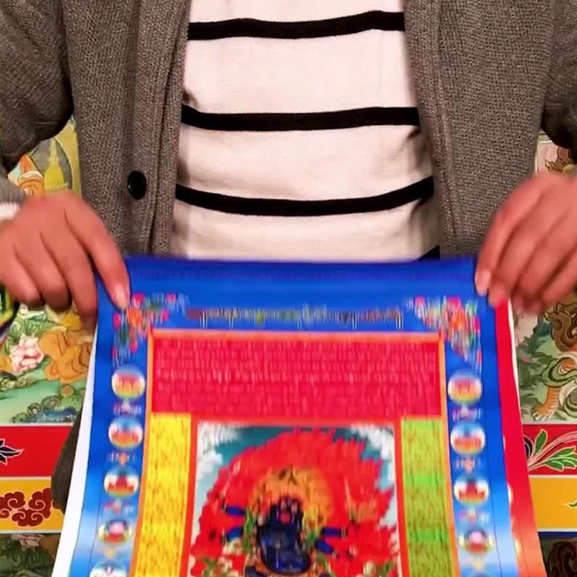 Tibetan windhorse prayer flag held by two hands at eye level, showcasing detailed printed artwork and sacred Buddhist imagery