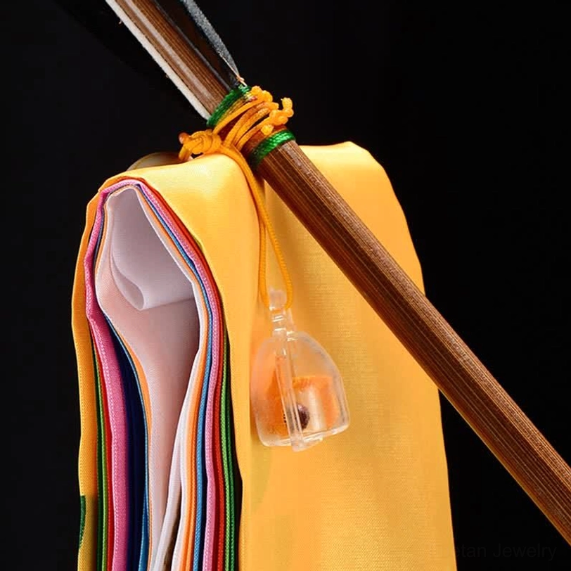 Tibetan prayer flag wooden pole mounting detail showing yellow binding rope, transparent hanging bell and folded colorful flags