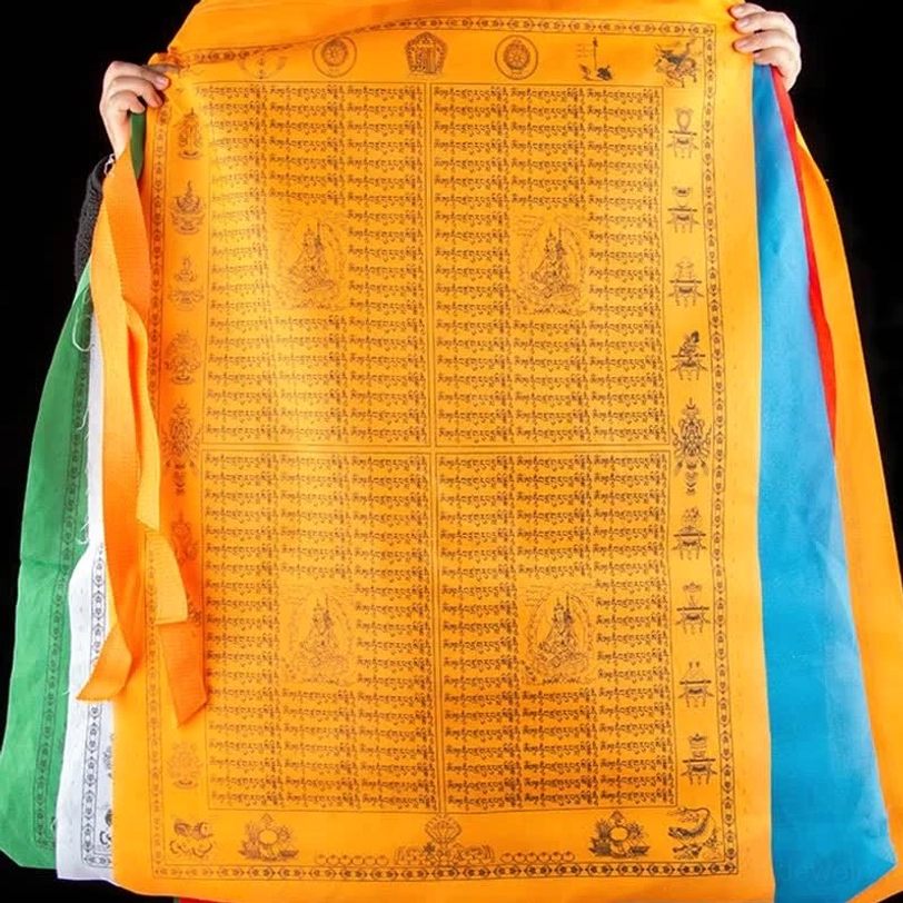 Tibetan prayer flag held up showing orange base with full-coverage black printed scriptures and vibrant multi-color fabric side decorations