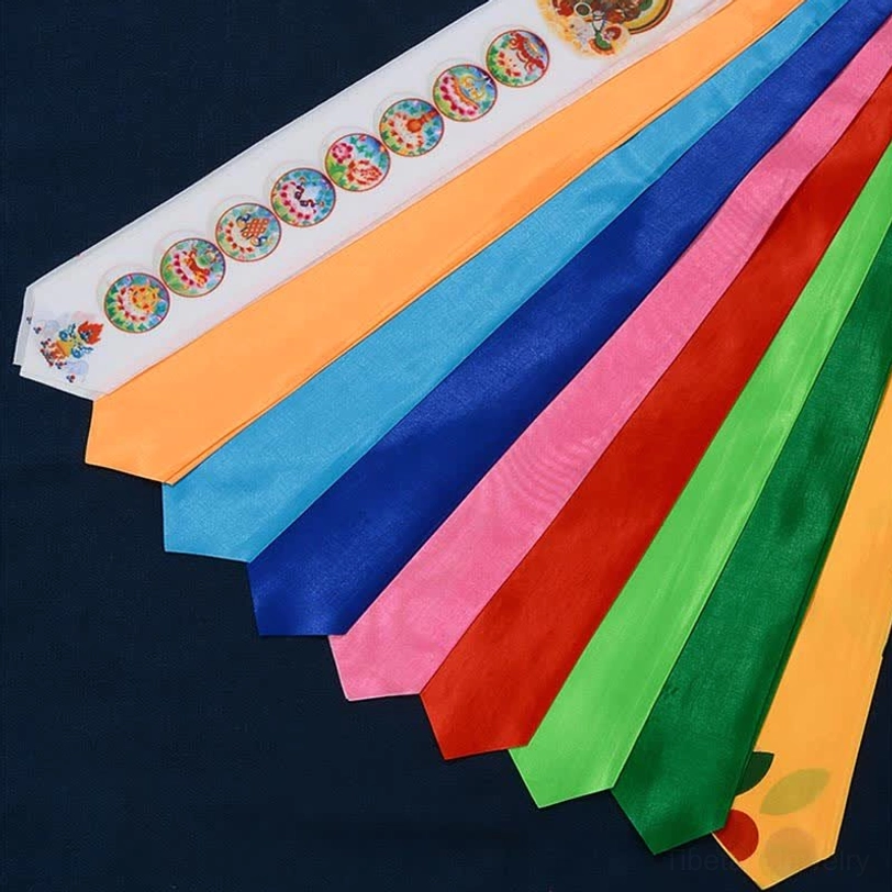 Assorted loose Tibetan prayer flag silk ribbons in bright five-sacred-colors layout on dark blue background, top-down view