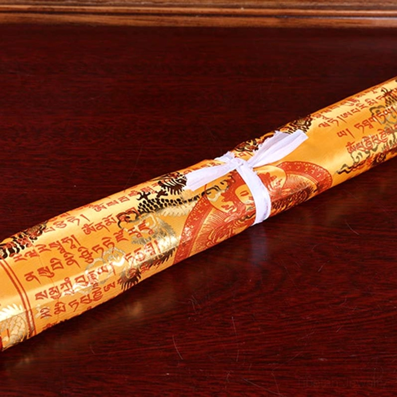 Single rolled tibetan prayer flag with golden base tied with white ribbon showing Buddhist design on wooden table surface