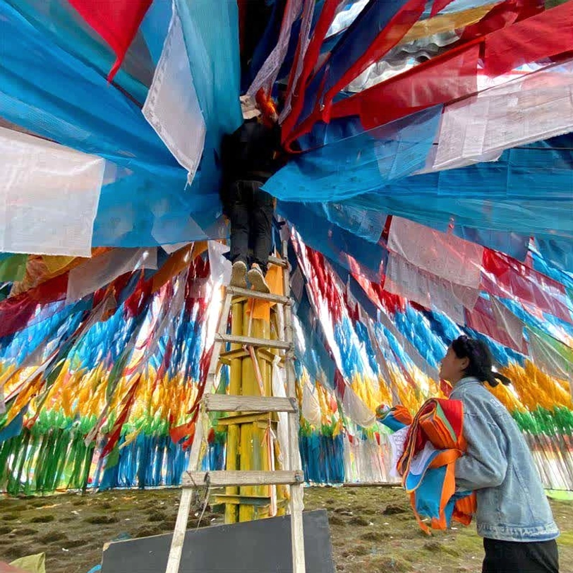 Tibetan 5-color prayer flags installation site with ladder construction and dense multicolor flag coverage