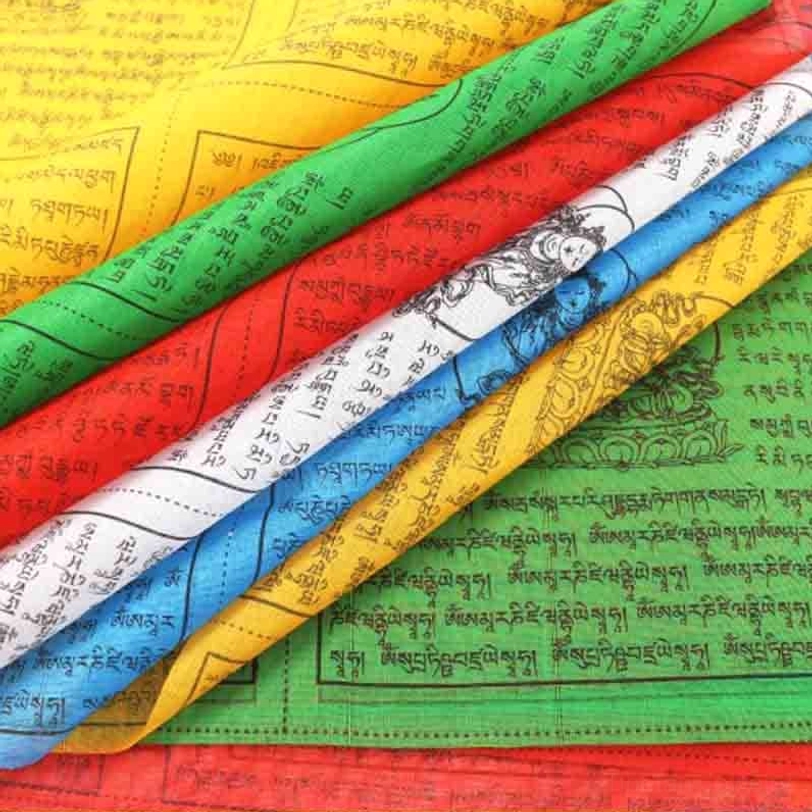 Close-up top view of folded Tibetan prayer flags showing colorful fabric with Buddha patterns and sacred Tibetan scriptures detail