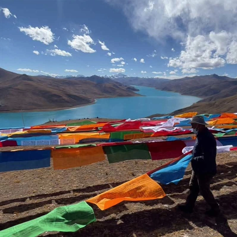 Traditional Tibetan prayer flags arranged at high altitude lakeside with artisan workers positioning strings