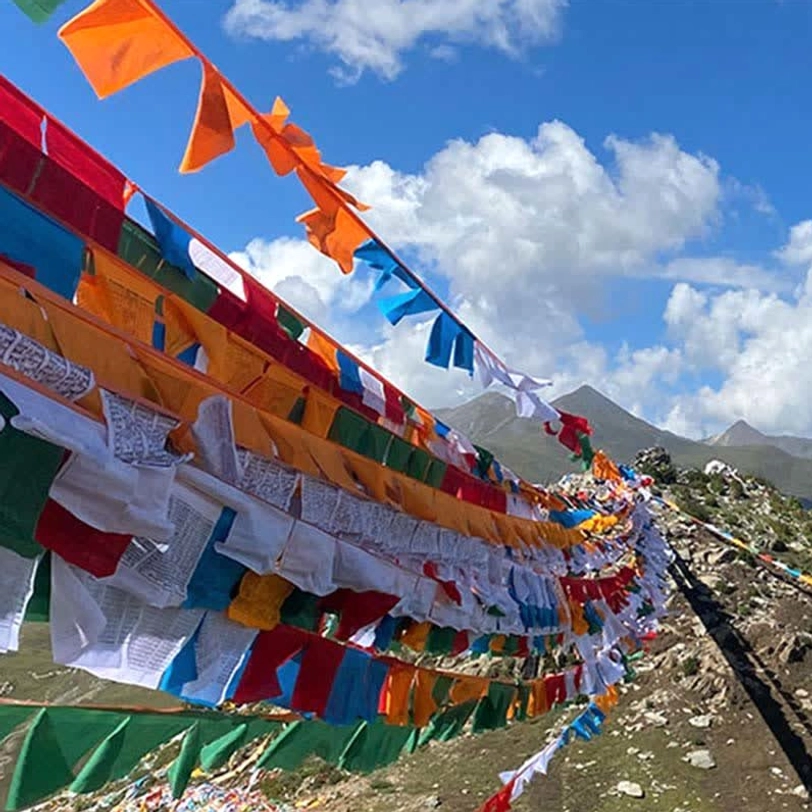 Tibetan windhorse prayer flags stacked on rocky alpine slope against cloudy mountain sky