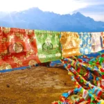 Tibetan 5-color windhorse prayer flags displayed outdoors against mountain backdrop, showing all five element colors strung across natural landscape