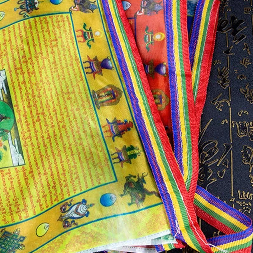 Partial stack of Tibetan prayer flags featuring woven rainbow borders and hand-printed Buddhist patterns