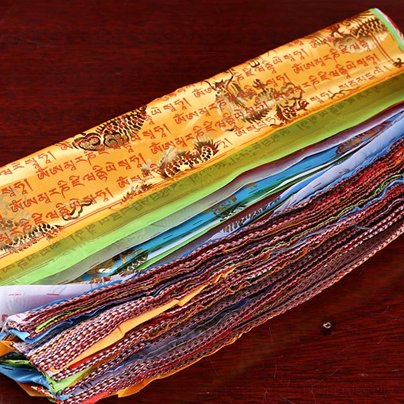 Stacked layered tibetan prayer flags flat lay showing multi-color fabrics with intricate tibetan sutras printed on dark wooden surface