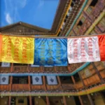 Tibetan prayer flags with Windhorse symbol hanging outdoors near traditional Tibetan building