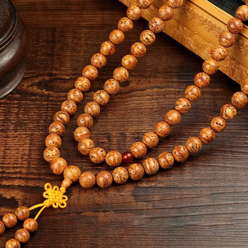 Bodhi seed prayer mala in three-quarter view on dark wood surface, displaying long strand with yellow tassel and red agate spacer beads