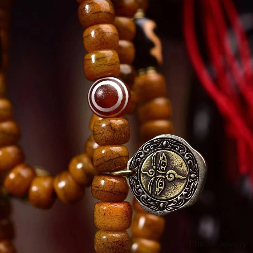 Tibetan mala bracelet side view showing tan bone beads, red agate accent bead, and carved copper pendant